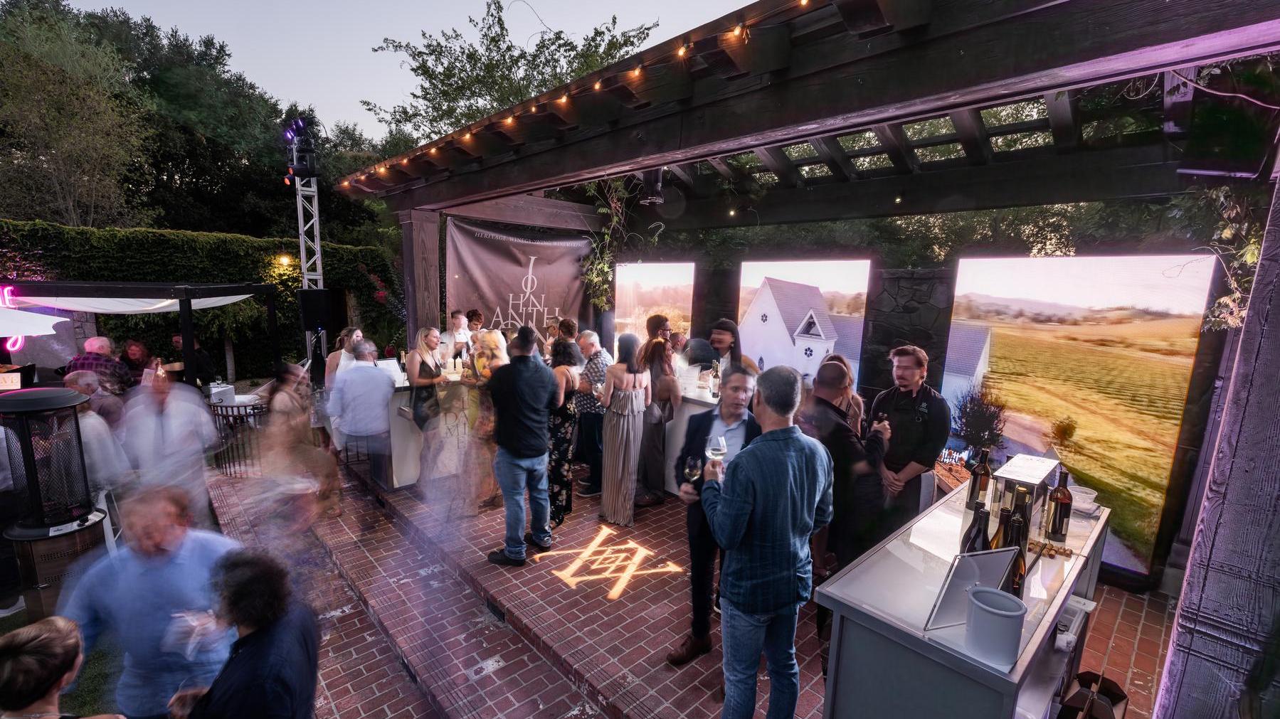 John Anthony Vineyards' activation at the V Foundation Wine Celebration, showcasing elegant wine bottles and branded signage under a canopy, where wine enthusiasts and philanthropists gather to support cancer research with special pourings and gourmet food pairings in the heart of Napa Valley.